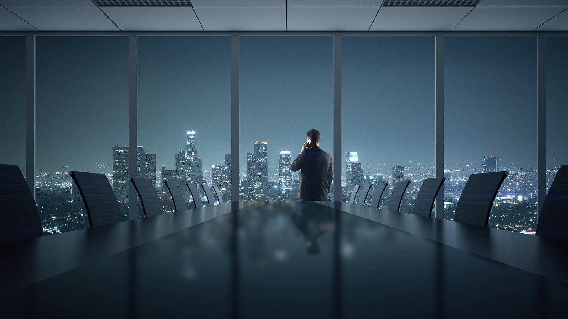 Figure on the phone at the window of a dark boardroom, city lights spread out below at night