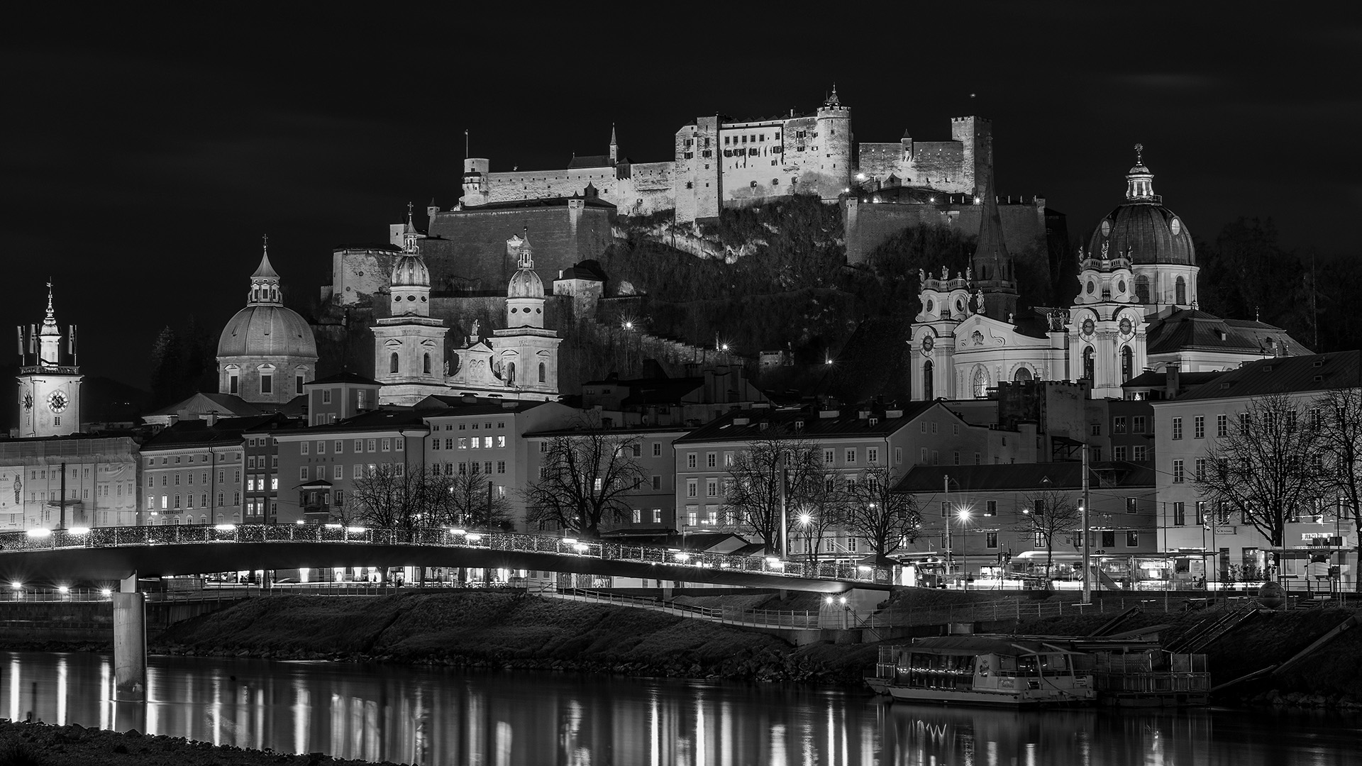 Hilltop fortress and domed old town lit at night above a river, in black and white
