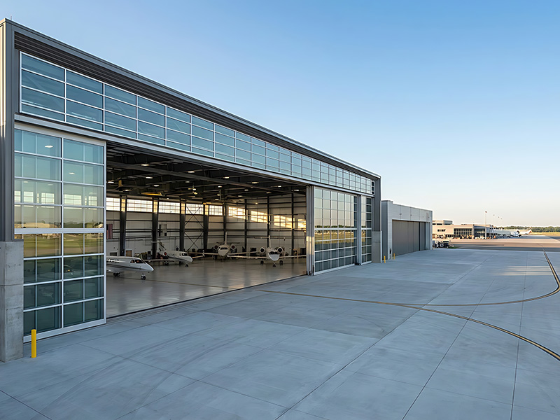 Open hangar door with private jets parked inside, seen from the apron at sunrise