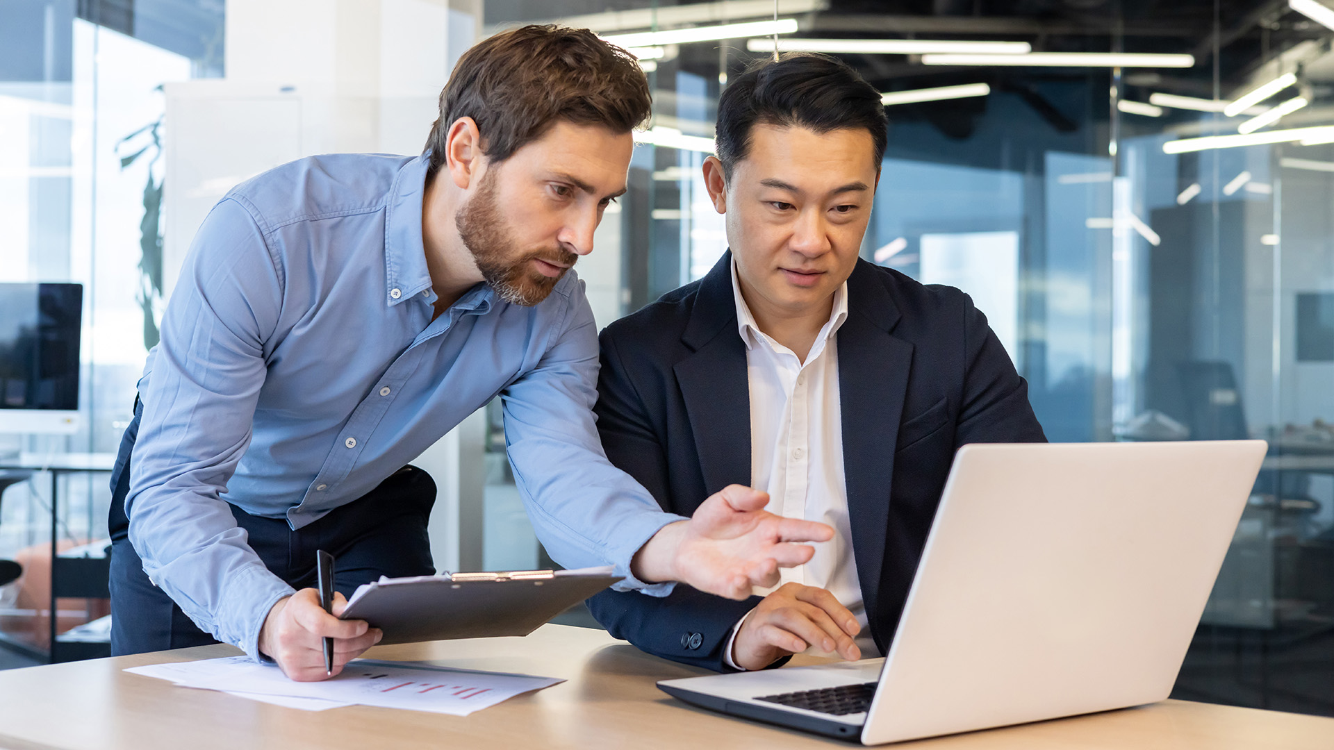 Two advisors reviewing a laptop together at a standing desk in a glass-walled office